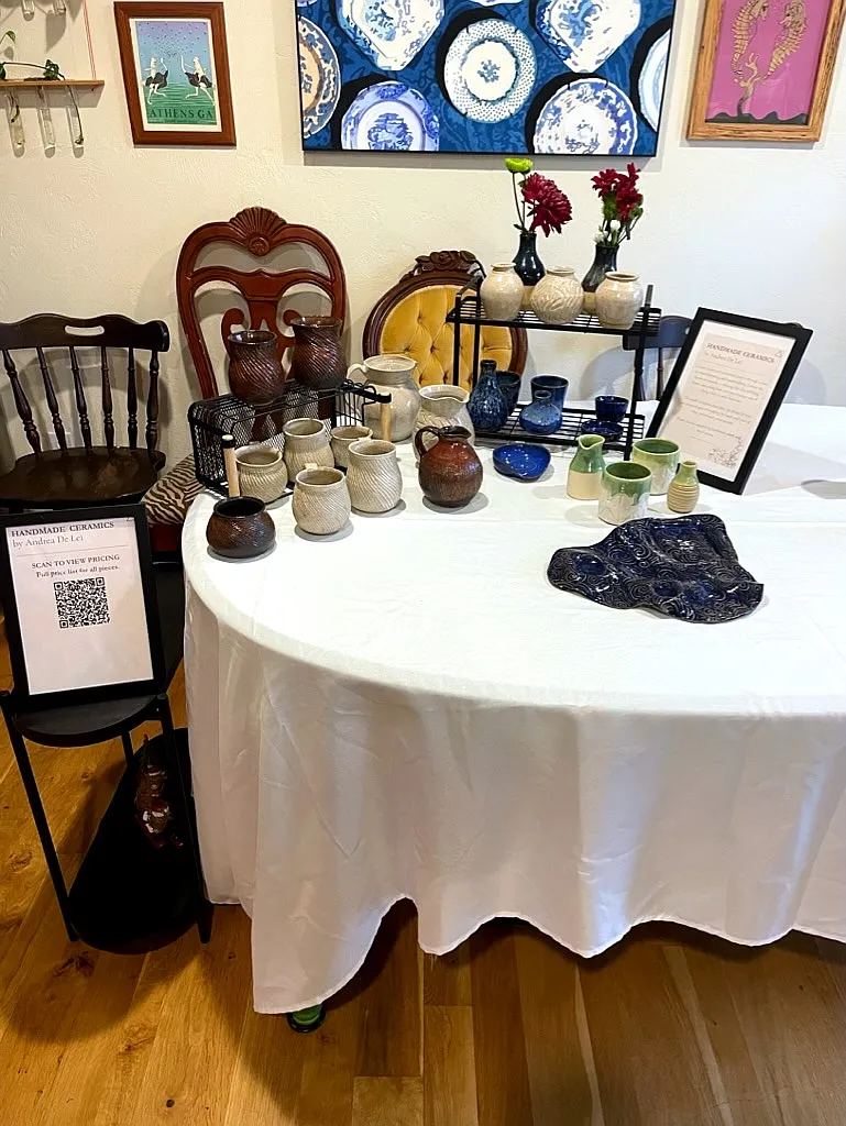 A market table of handmade ceramics: vases, mugs, pitchers, and a carved blue platter