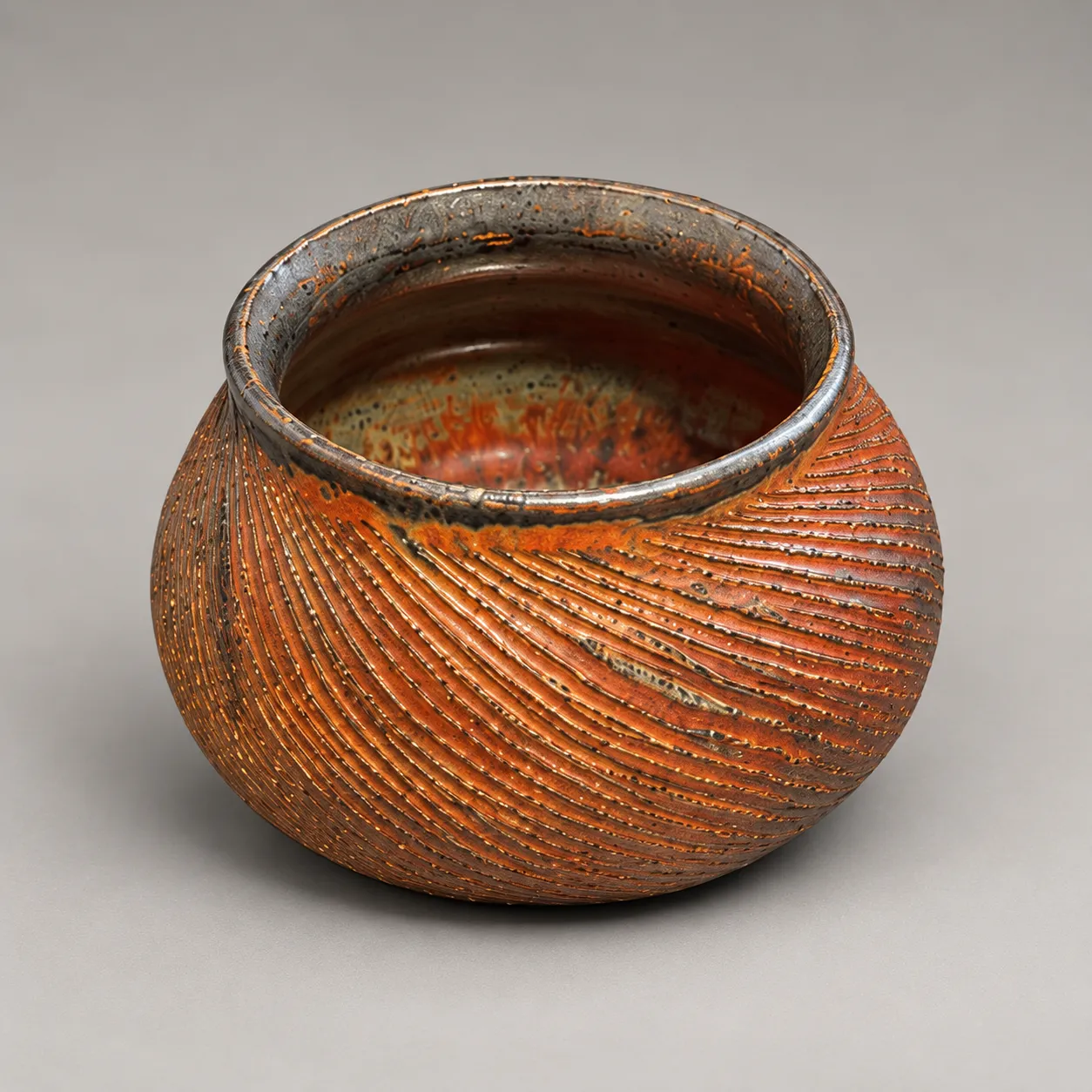 Round carved vessel with rolled gunmetal rim in copper-red metallic glaze
