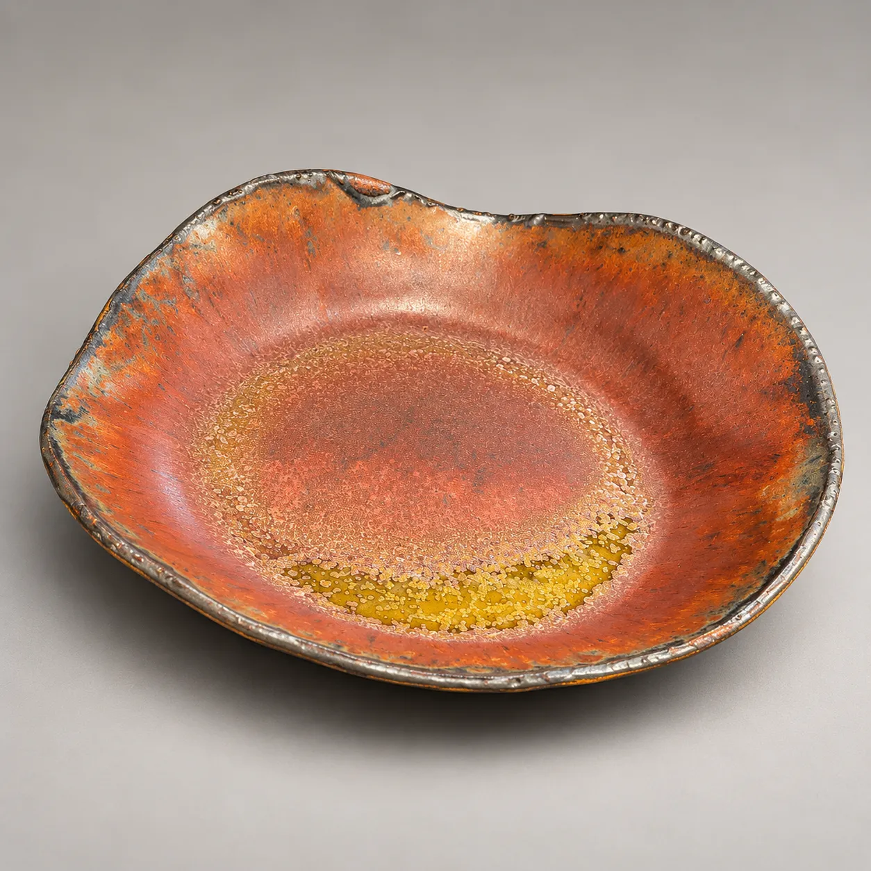 Irregular rimmed plate in copper-red metallic glaze pooling to amber in the center