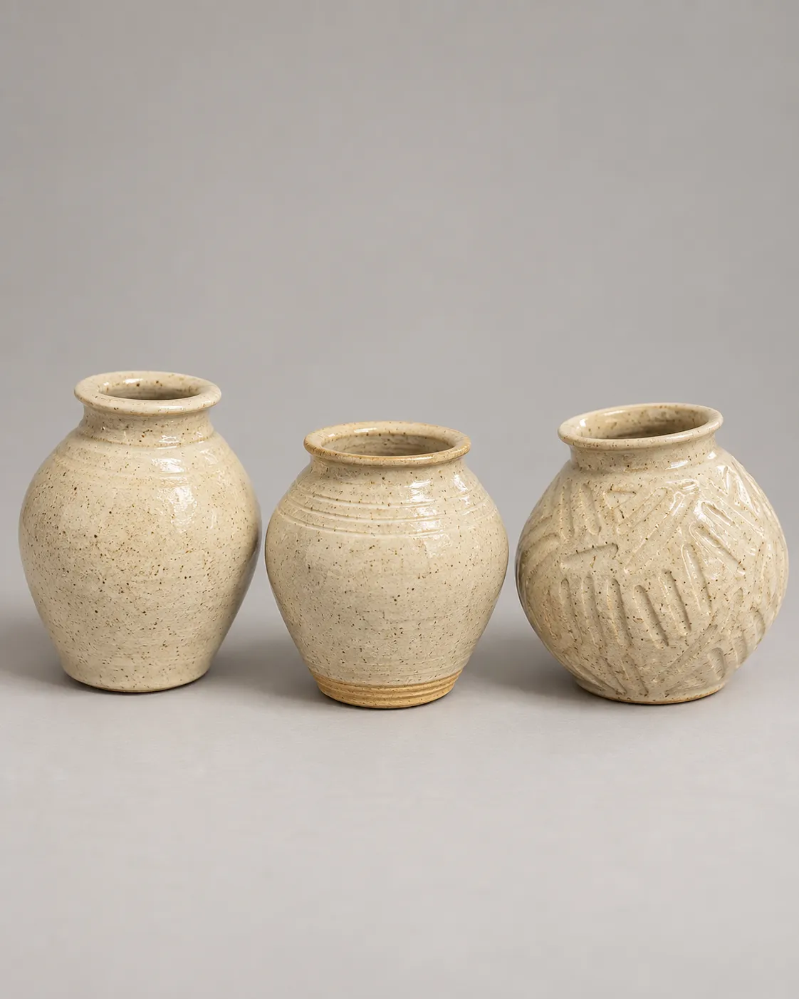 Three small speckled cream vases: smooth, ringed, and carved
