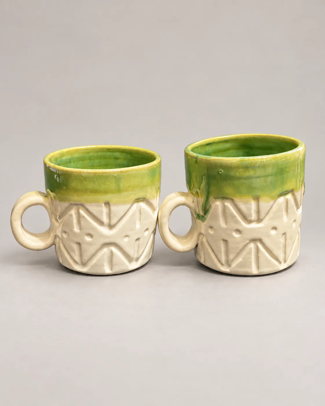 Two cream mugs with carved zigzag bands, ring handles, and green glazed rims