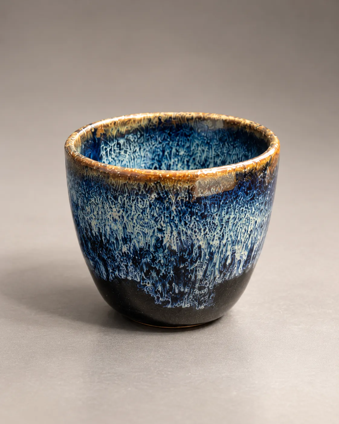 Rounded cup in variegated blue glaze fading to near-black at the base, amber rim