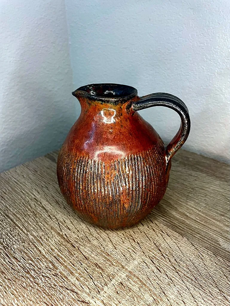 A round terracotta pitcher with carved base and dark glazed rim
